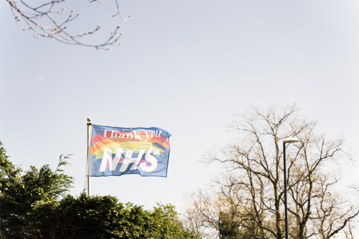 NHS thank you flag above trees with sky in the background.